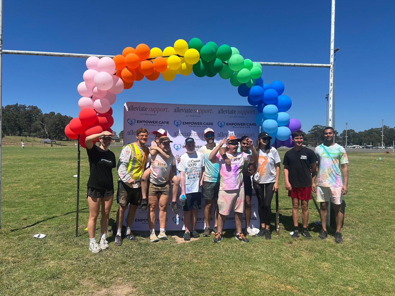 A big group covered in coloured powder under the rainbow balloon arch at the Colour Run, Jamison Park, 9 October 2026.