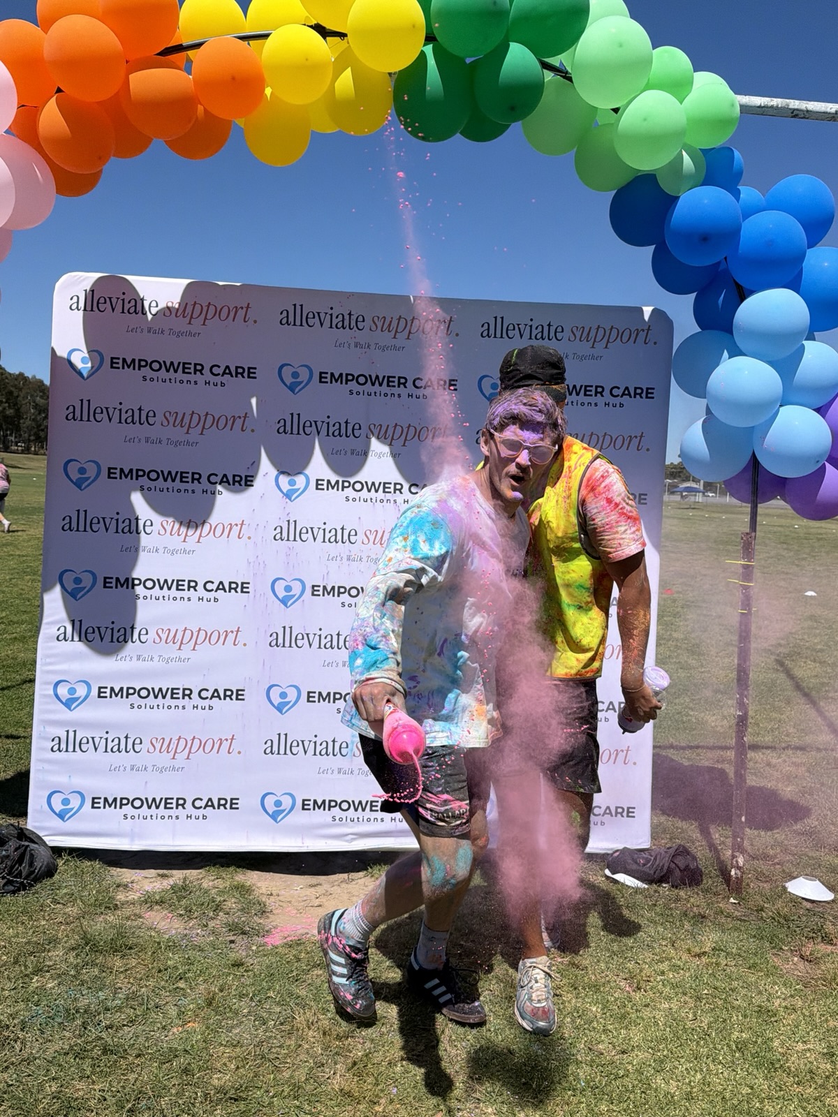 Coloured powder flying in front of the Empower and Alleviate Support backdrop