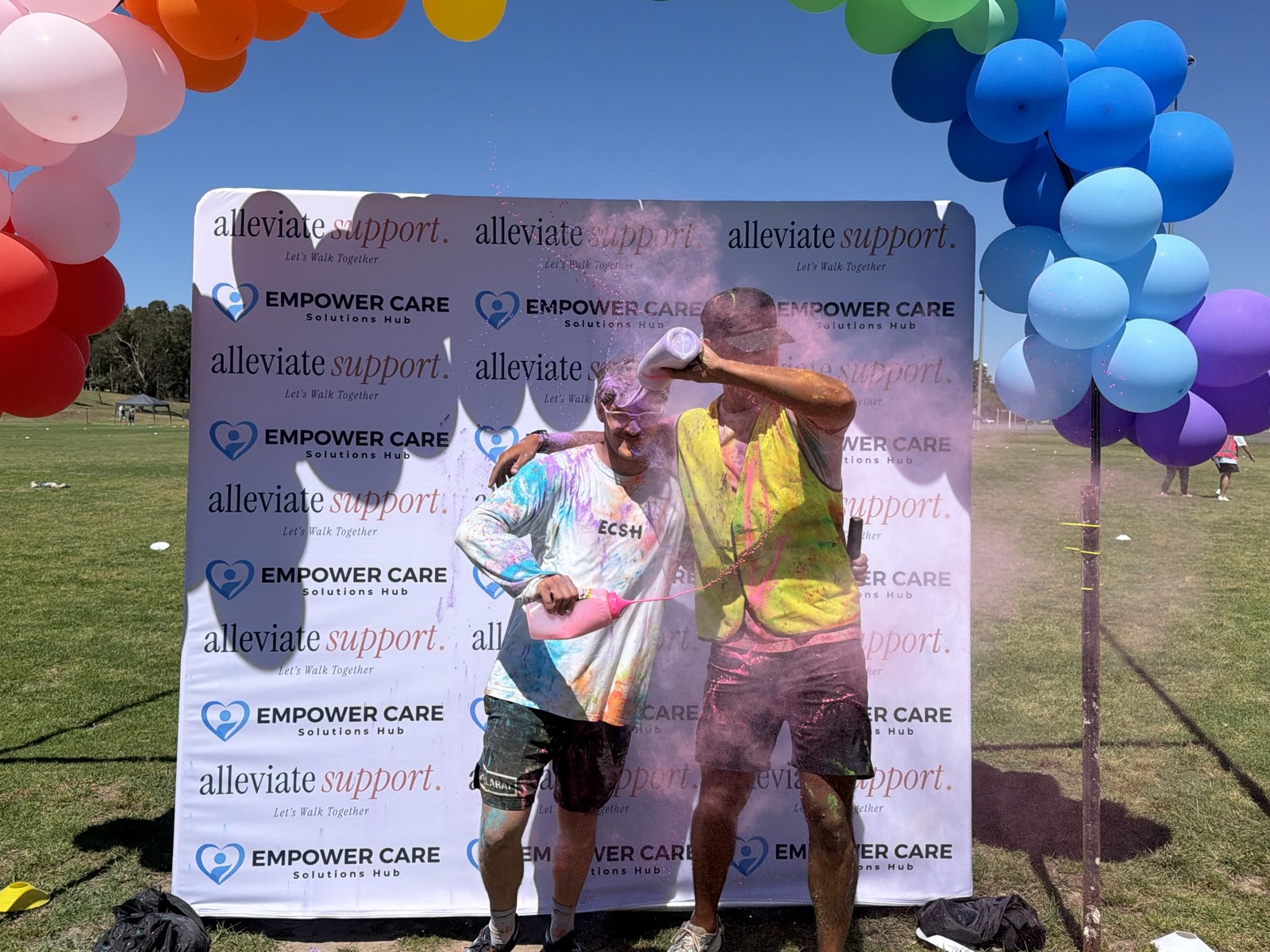 Two of the team being showered in pink and blue powder at the Colour Run photo wall, 9 October 2026.